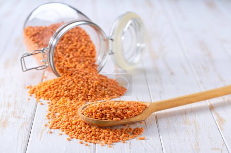 Photo for Organic red lentils in wooden scoop and in glass storage jar on a light table, selective focus. - Royalty Free Image