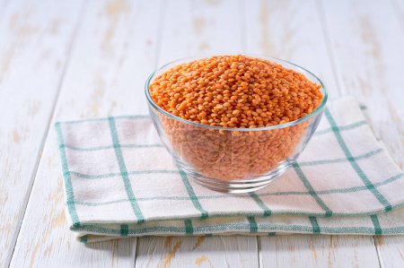 Photo for Organic red lentils in a clear glass bowl on a light table, selective focus. - Royalty Free Image
