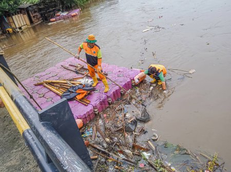 Téléchargez les photos : Jakarta, Indonésie - 24 février 2023 : Deux nettoyeurs démêlent les ordures coincées sous le pont. La forte intensité de la pluie dans la région de Jakarta a provoqué le débordement du Sungai Banjir Kanal Barat. - en image libre de droit