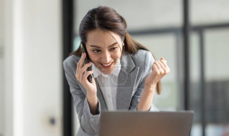 Téléchargez les photos : Jeune souriant heureux excité entreprise asiatique femme parler sur téléphone mobile, debout dans le bureau de travail avec document dans sa main - en image libre de droit