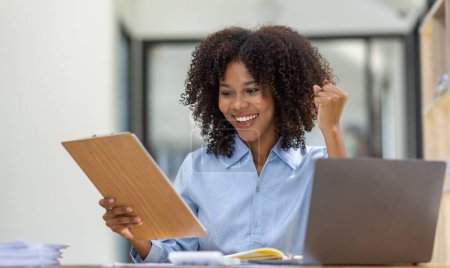 Téléchargez les photos : Heureuse femme africaine asiatique excitée regardant l'écran de l'ordinateur portable, célébrant une victoire en ligne, ravie jeune fille africaine criant de joie, isolée sur un fond de bureau - en image libre de droit