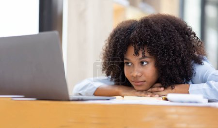 Foto de Mujer africana agotado milenario durmiendo en su escritorio de la oficina, al lado de la computadora portátil y documentos, cansado de exceso de trabajo. Niña africana joven adicta al trabajo que sufre de fatiga crónica en el lugar de trabajo - Imagen libre de derechos