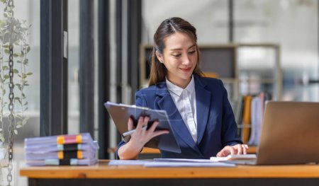 Téléchargez les photos : Brun veste bleu clair souriant femme asiatique travailler avec document ordinateur portable au bureau, faire la planification de l'analyse du rapport financier, investissement du plan d'affaires, concept d'analyse financière. - en image libre de droit
