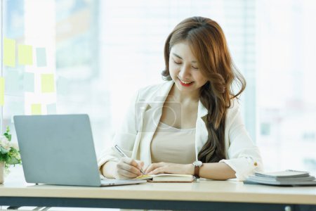 Téléchargez les photos : Souriant Mignon asiatique femme portable de travail heureux pour le succès. Attrayant Happy employée dans le bureau ou espace de co-travail avec espace de copie pour le texte de l'étiquette. - en image libre de droit