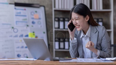 Téléchargez les photos : Heureux heureux heureux succès asiatique femme d'affaires triomphant avec smartphone et ordinateur portable sur le lieu de travail. - en image libre de droit