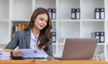 Téléchargez les photos : Belle jeune femme asiatique souriante multiethnique travaillant sur ordinateur portable et buvant du café sur le lieu de travail, Asie femme document de travail finance et calculatrice dans son bureau à la maison. Profiter du temps à la maison. - en image libre de droit