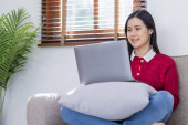 Happy casual beautiful Asian woman is talking on a laptop computer sitting on a sofa at home. t-shirt #625552666