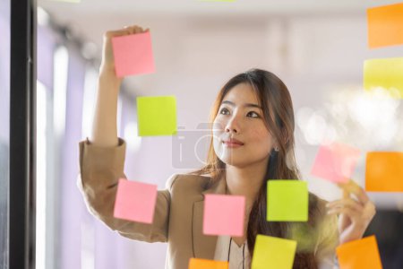 Téléchargez les photos : Share idea, project successful, Business Asian business woman in meeting brainstorming and use post paper and writing note and stick on glass wall at workplace office. - en image libre de droit