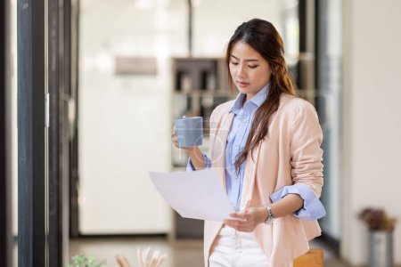 Téléchargez les photos : Portrait of a charming young woman businessman in the office standing holding a Coffee cup in hand and looking away from camera - en image libre de droit
