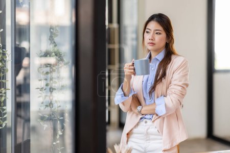 Téléchargez les photos : Portrait of a charming young woman businessman in the office standing holding a Coffee cup in hand and looking away from camera - en image libre de droit