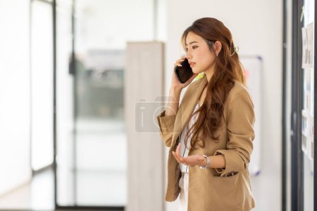 Téléchargez les photos : Young Office Asian Woman Talking to Someone on her Mobile Phone While Looking Into the Distance with Happy Facial Expression. - en image libre de droit