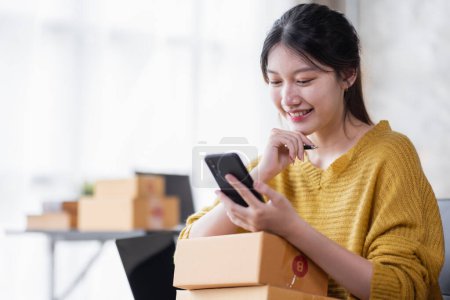 Téléchargez les photos : Startup SME small business entrepreneur of freelance Asian woman using a laptop with box Cheerful success Asian woman her hand lifts up online marketing packaging box and delivery SME idea concept - en image libre de droit