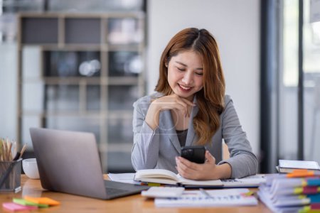 Téléchargez les photos : Smiling young Asian business woman executive looking at smartphone using cellphone mobile cell tech, happy ethnic professional female worker working in office typing on cellphone sitting at desk. - en image libre de droit