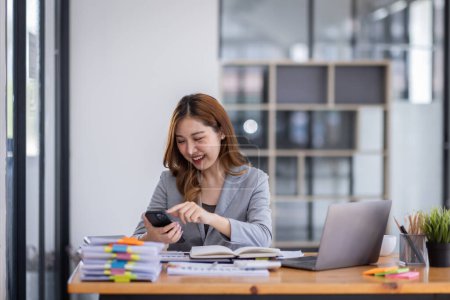 Téléchargez les photos : Smiling young Asian business woman executive looking at smartphone using cellphone mobile cell tech, happy ethnic professional female worker working in office typing on cellphone sitting at desk. - en image libre de droit