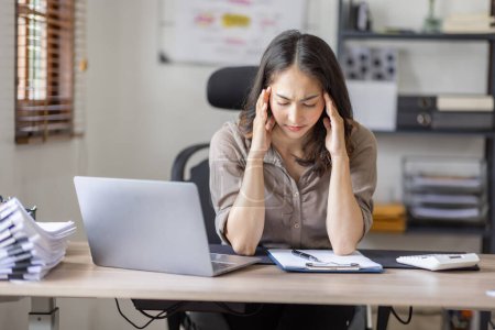 Foto de Asian indian women are stressed while working on laptop, Tired asian businesswoman with headache at office, feeling sick at work copy space in workplace an home office. - Imagen libre de derechos