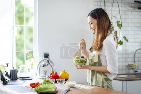 Téléchargez les photos : Portrait of attractive asian japanese woman in kitchen at home, young girl browsing website on tutor cooking class and doing for kitchen, cutting vegetables, cooking, cooking concept. - en image libre de droit