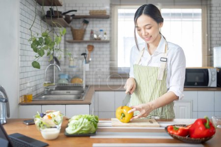 Téléchargez les photos : Portrait of attractive asian japanese woman in kitchen at home, young girl browsing website on tutor cooking class and doing for kitchen, cutting vegetables, cooking, cooking concept. - en image libre de droit