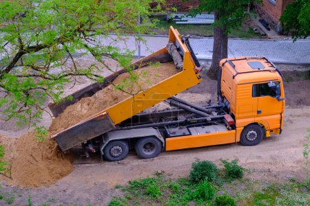Téléchargez les photos : Un grand camion à benne orange décharge le sable - en image libre de droit