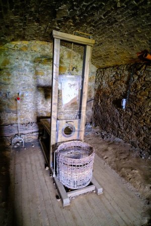 Foto de Hay poca luz en el cuarto oscuro del sótano. La guillotina, una herramienta medieval de castigo, se levanta con una cesta hecha de mimbre. - Imagen libre de derechos