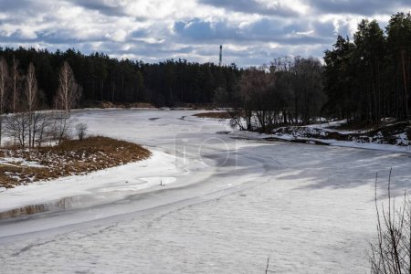 Eine ruhige Winterlandschaft mit einem gefrorenen Fluss, umgeben von dichtem Wald