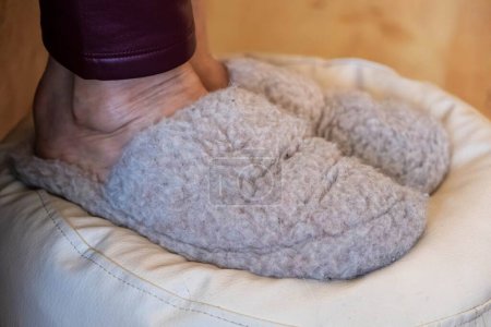 A person feet in soft woolen slippers, resting on a cushioned seat