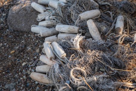 Red de pesca descartada y botellas de plástico que contaminan una playa rocosa.