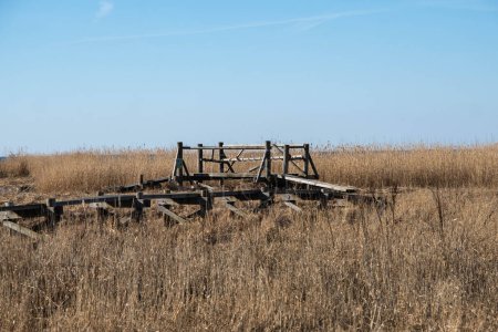 Eine verlassene, verfallene Holzstruktur in einem riesigen, trockenen Grasfeld unter klarem Himmel.