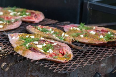 Marinated fish steaks grilling with herbs and spices outdoors.