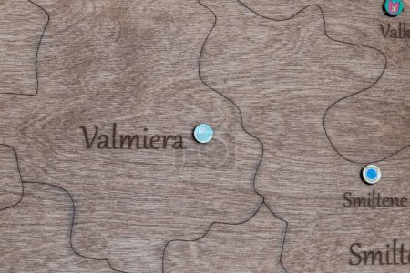 A detailed wooden map with engraved outlines and names of towns, highlighting Valmiera with a marker, showcasing craftsmanship and geographical interest.