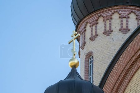 Gros plan d'un dôme d'église orthodoxe surmonté d'une croix d'or, mettant en valeur des briques complexes contre un ciel bleu clair.