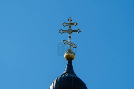 Close-up of an ornate church cross atop a domed roof, set against a clear blue sky, symbolizing faith and spirituality.