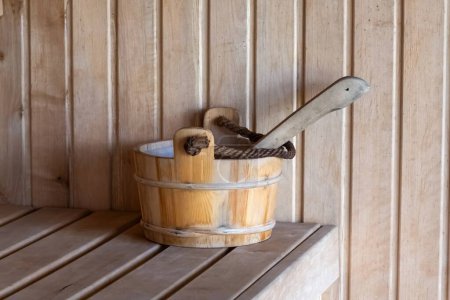 Close-up of a wooden bucket and ladle placed on a bench inside a traditional sauna, highlighting the rustic spa experience.