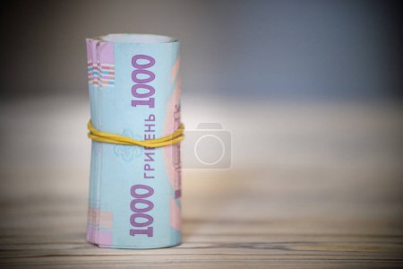 nueva hryvnia ucraniana. 1000 hryvnia en la mesa de madera se unen con cinta de goma al tubo. dinero fondo y concepto de riqueza.