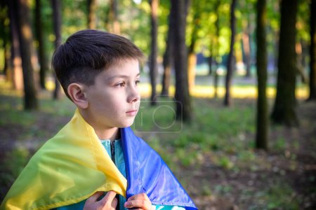 Foto de Un adolescente patriota preocupado lleva una bandera azul amarilla ucraniana sobre sus hombros. Fondo de la naturaleza primavera. Ucrania símbolo nacional. Patriotismo. - Imagen libre de derechos