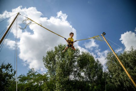 Photo for The boy is jumping on a bungee trampoline. A child with insurance and stretchable rubber bands hangs against the sky. The concept of happy childhood and games in the amusement park. - Royalty Free Image