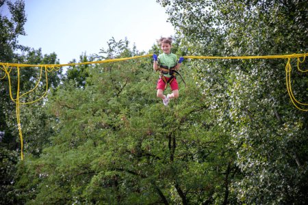 Photo for The boy is jumping on a bungee trampoline. A child with insurance and stretchable rubber bands hangs against the sky. The concept of happy childhood and games in the amusement park. - Royalty Free Image