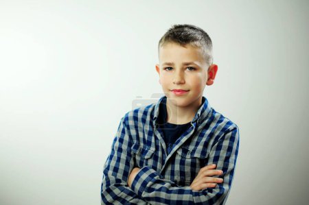 Photo for Satisfied smiling caucasian kid boy wearing plaid shirt over white background, smiling schoolboy in a plaid shirt stands with his arms crossed on his chest - Royalty Free Image