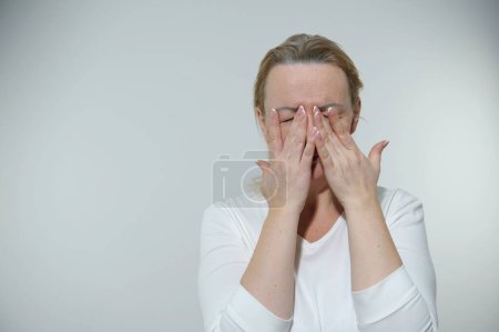 Foto de 40-50 years old adult real woman is crying she covered face with hands she has French manicure but tired expression she is on white background in compassion sadness tiredness needs rest - Imagen libre de derechos