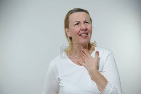 Photo for Sore throat vocal cords tense woman cant speak she sticks out tongue looks up wrinkled hand holds throat cant say word real person treatment medicine scratchy throat swallowed choked 40-50 years old - Royalty Free Image