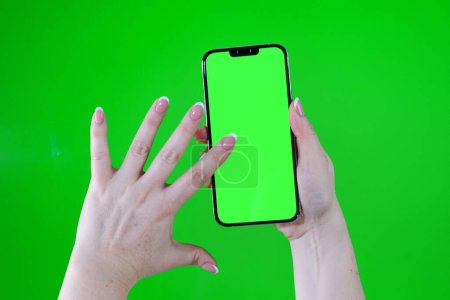 Foto de Woman holds phone with green screen on which there can be advertisement for any product technology Internet online shopping typing search Internet for desired product gt1 with finger swipes - Imagen libre de derechos