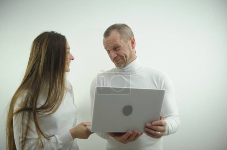 Foto de Bosses subordinates in office look at each other in hands of laptop man is surprised smile adult woman young laughs man asks Is it really serious white background white clothes online purchase - Imagen libre de derechos