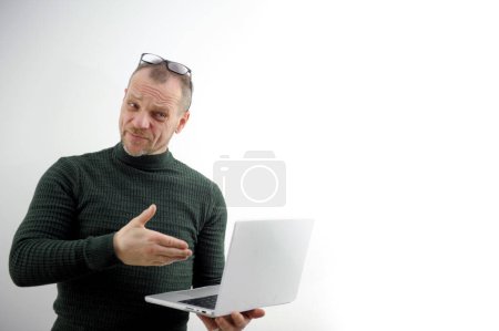 Foto de Adult man persistently offers project to raise glasses to forehead to hold laptop hands white background shows hand to technological device offering wrinkled forehead furrowed eyebrows beard mustache - Imagen libre de derechos