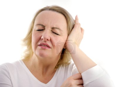 Kopfschmerzen erwachsene Frau mittleren Alters stört Lärm sie schließt ihre Ohren Schielen ihre Augen gebeugt mit einem unzufriedenen Gesicht tut Kopfschmerzen im Ohr weißen Hintergrund weiße Jacke unangenehm