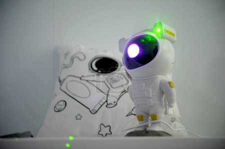 Téléchargez les photos : Fond pour le texte enfants jouets détente robot jouet lampe projecteur lumière rayonner lumière verte lampe place pour la publicité carte postale oreiller blanc avec photo d'étoiles astronaute et fusées - en image libre de droit