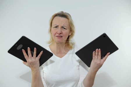 Photo for Woman has two tablets in hands she is unhappy looks into frame tired of work an overabundance of information burnt out at work white background white clothes Studio no dyed hair no time for yourself - Royalty Free Image