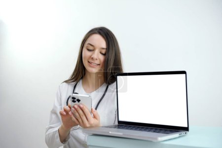 Photo for Side view portrait of young female doctor speaking by phone while sitting at desk and working in clinic or hospital, copy space. High quality photo - Royalty Free Image