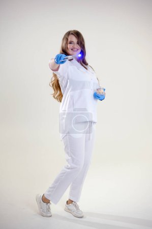 Foto de Doctor con una varita mágica en guantes de látex azul. Mujer en traje médico blanco con reloj inteligente con cabello suelto evoca un tratamiento. inventa tratamientos anuncios de suplementos sabrosos medicamentos - Imagen libre de derechos