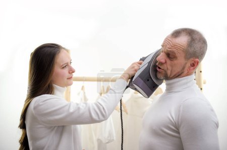 Photo for Man and a woman have fun a woman puts an iron on her husbands cheek to measure the temperature with an iron to torture him to show him who is the boss in the house the woman the main man obeys - Royalty Free Image