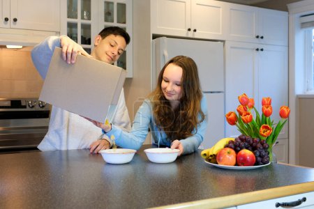 Photo for Teenagers boys and girl cooking Breakfast poured from a box of cereal on the box can Your advertising empty space for text space delicious food spend time together fun brother and sister - Royalty Free Image