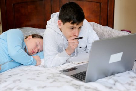 Téléchargez les photos : Adolescents assis à des ordinateurs font des devoirs étude en ligne et ne sont pas fatigués d'étudier aller au lit s'endormir L'un travaille l'autre dort aucun désir d'étudier les yeux mal besoin de se reposer - en image libre de droit